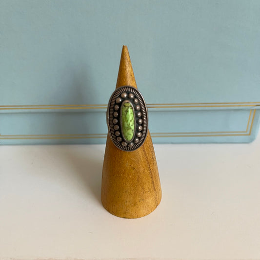 Ring with a green stone and silver band on a wooden cone against a light blue background