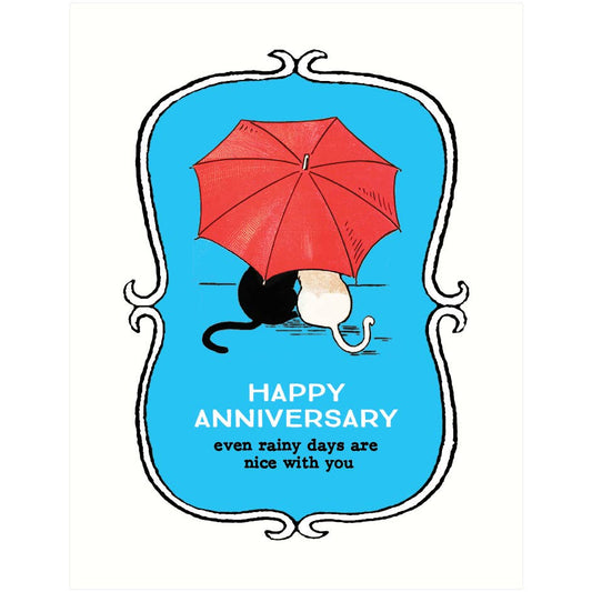 A square greeting card or print with a white border and a central blue decorative frame. The illustration shows a red umbrella over a black-and-white cat, with the text 'HAPPY ANNIVERSARY even rainy days are nice with you'.