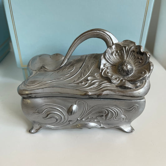 Decorative silver jewelry box with floral design on a white surface