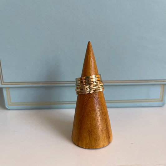 Wooden cone-shaped ring holder with 8 gold rings on a light blue background