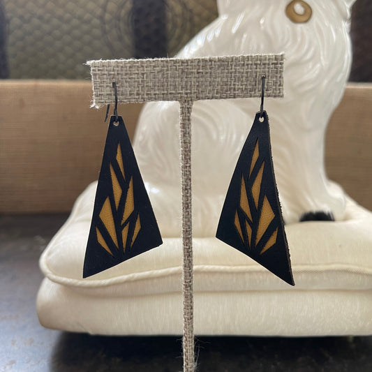 Black and brown leather geometric drop earrings on a display stand with a blurred background