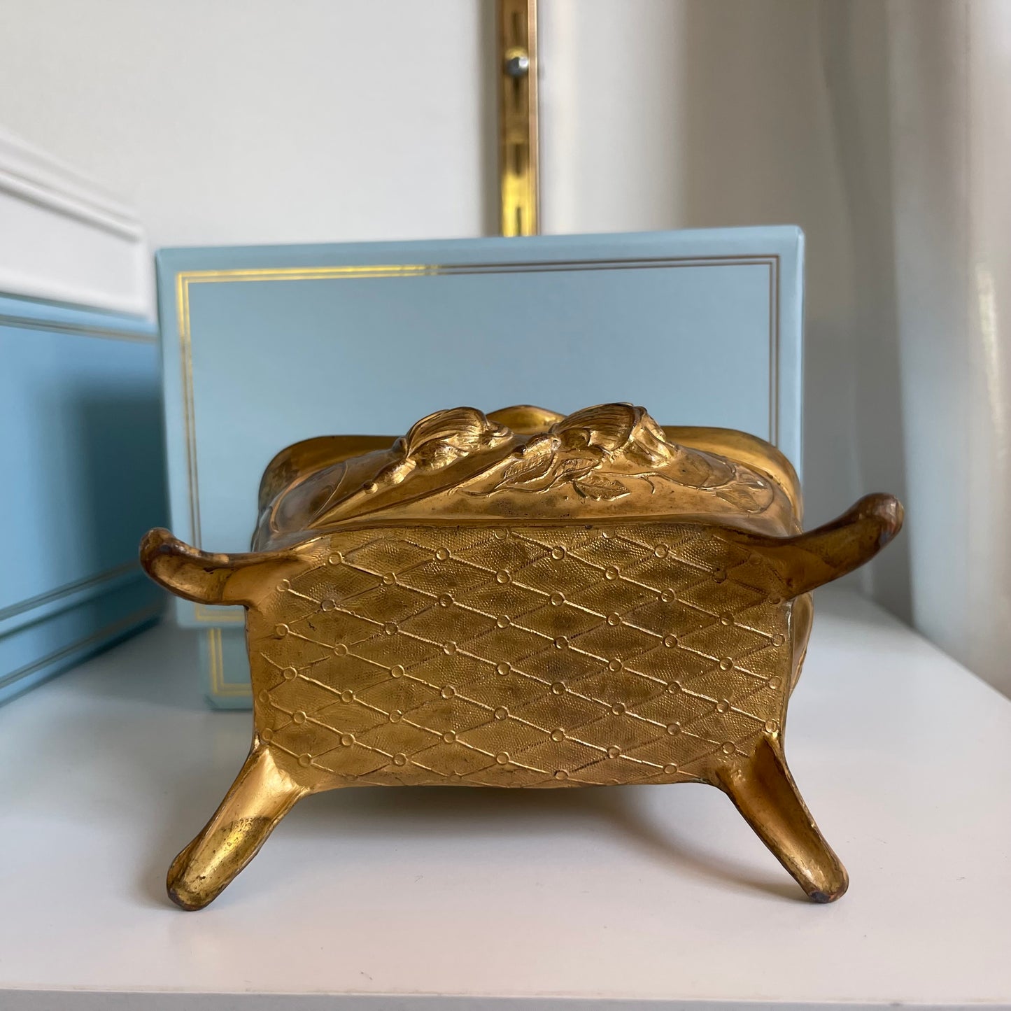 Gold decorative jewelry box bottom on a white surface with a light blue box in the background