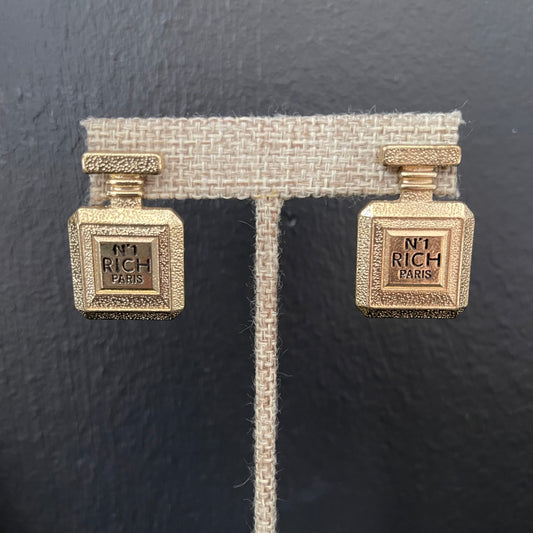 Gold perfume bottle-shaped earrings on a black background