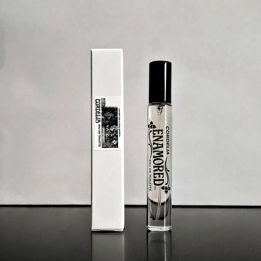 A clear glass perfume bottle with a black cap stands next to its white rectangular box. The bottle and box are printed with the brand name 'ENAMORED' and the scent name 'CORDELIA' in black text, with a small floral graphic.