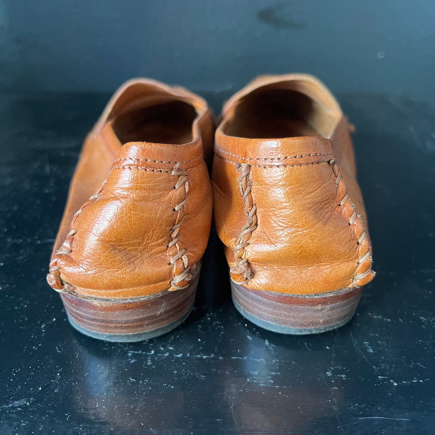 Backs of chestnut brown penny loafers with white stitching and slightly darker brown heels