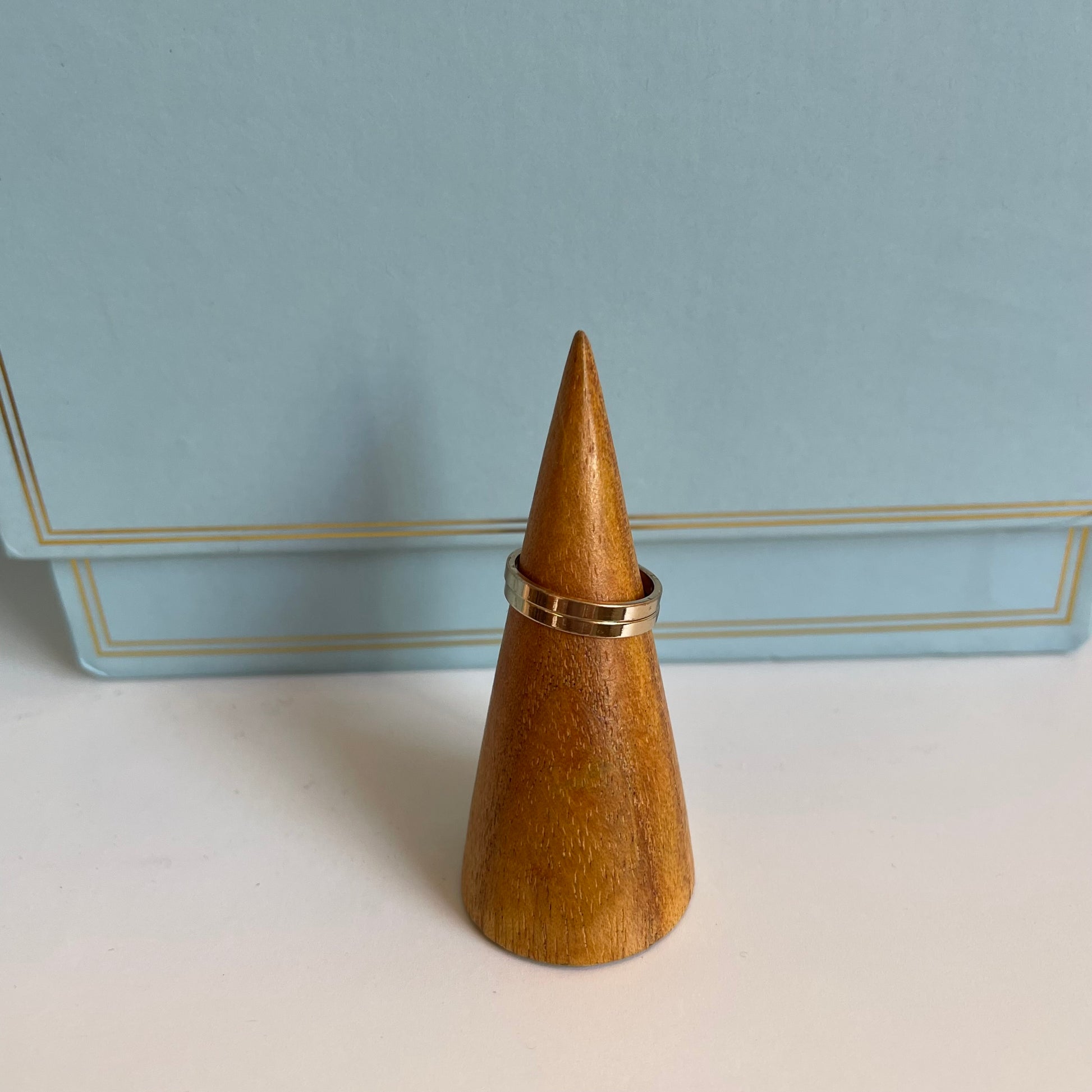 Wooden cone-shaped ring holder with two gold rings on a light blue background