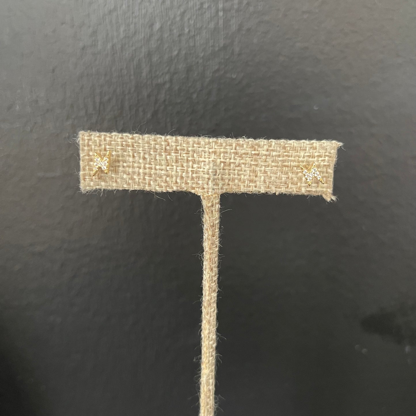 Small lightening-shaped stud earrings on a burlap fabric earring display against black background
