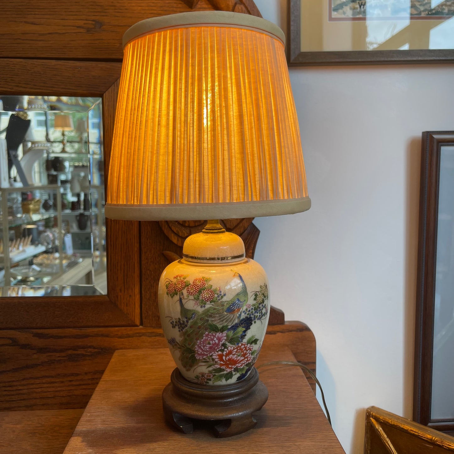A vintage-style ceramic table lamp with a pleated warm yellow-gold shade and a hand-painted multicolor floral and bird base, sitting on a wooden table in an indoor setting.