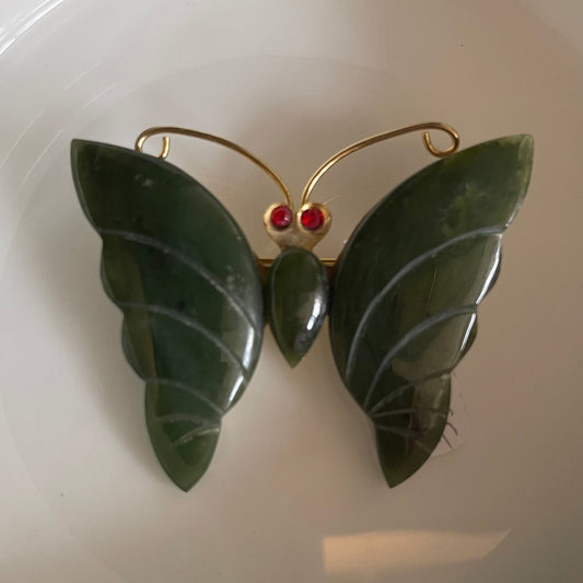 Green butterfly-shaped brooch with red jeweled eyes on a white plate