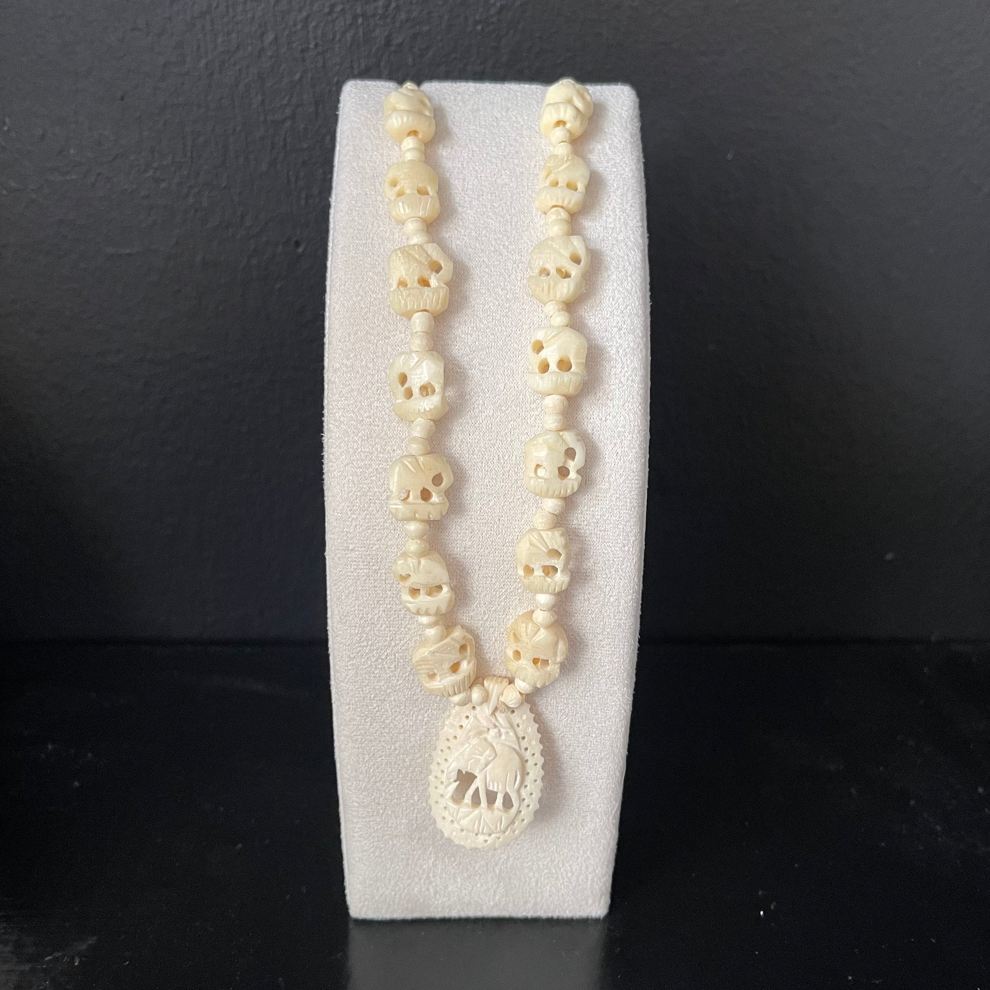 Necklace with ivory elephant beads with carved elephant pendant on a white stand against a dark background