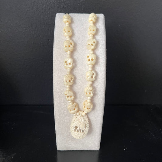 Necklace with ivory elephant beads with carved elephant pendant on a white stand against a dark background