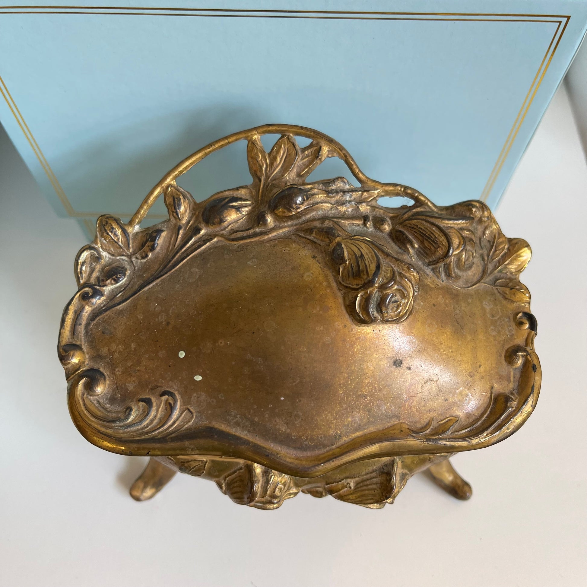 Decorative gold jewelry box lid with intricate designs on a light blue background