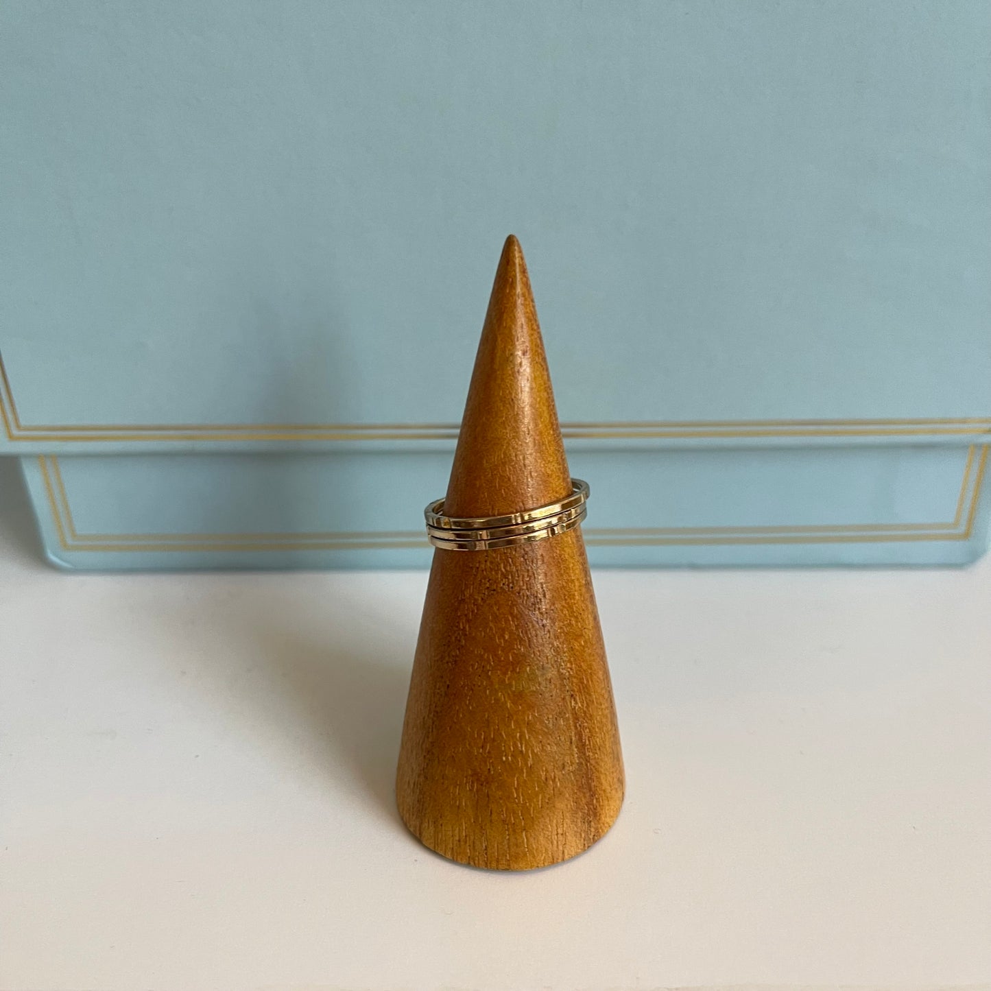 Wooden cone-shaped ring holder with 3 thin gold rings on a light blue background