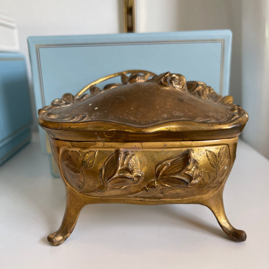 Decorative gold jewelry box with floral designs on a white surface