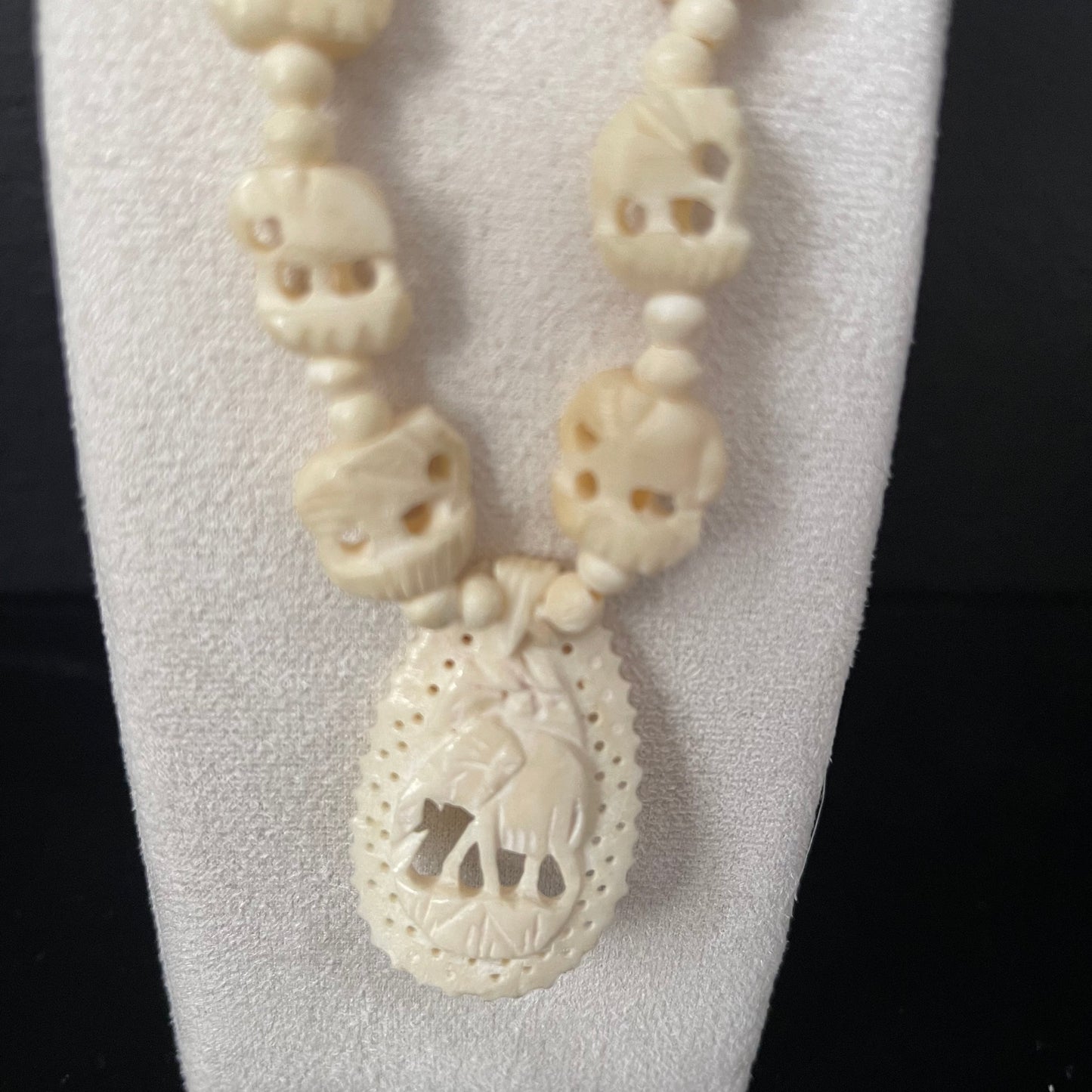 Ivory necklace with teardrop pendant with carved elephant on a white stand against a black background