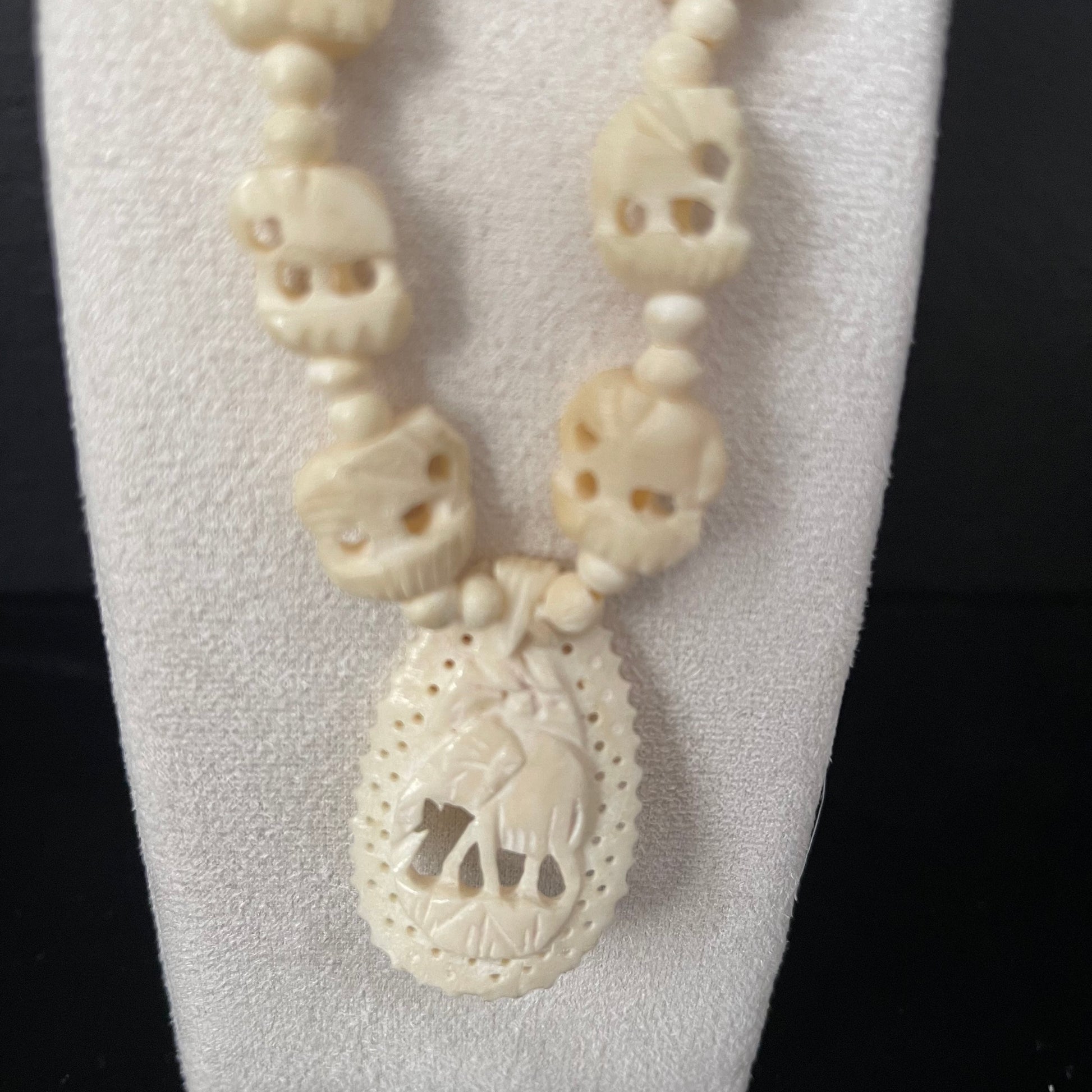 Ivory necklace with teardrop pendant with carved elephant on a white stand against a black background