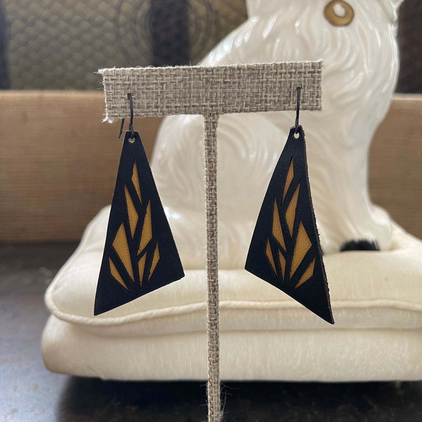 Black and brown leather geometric drop earrings on a display stand with a blurred background