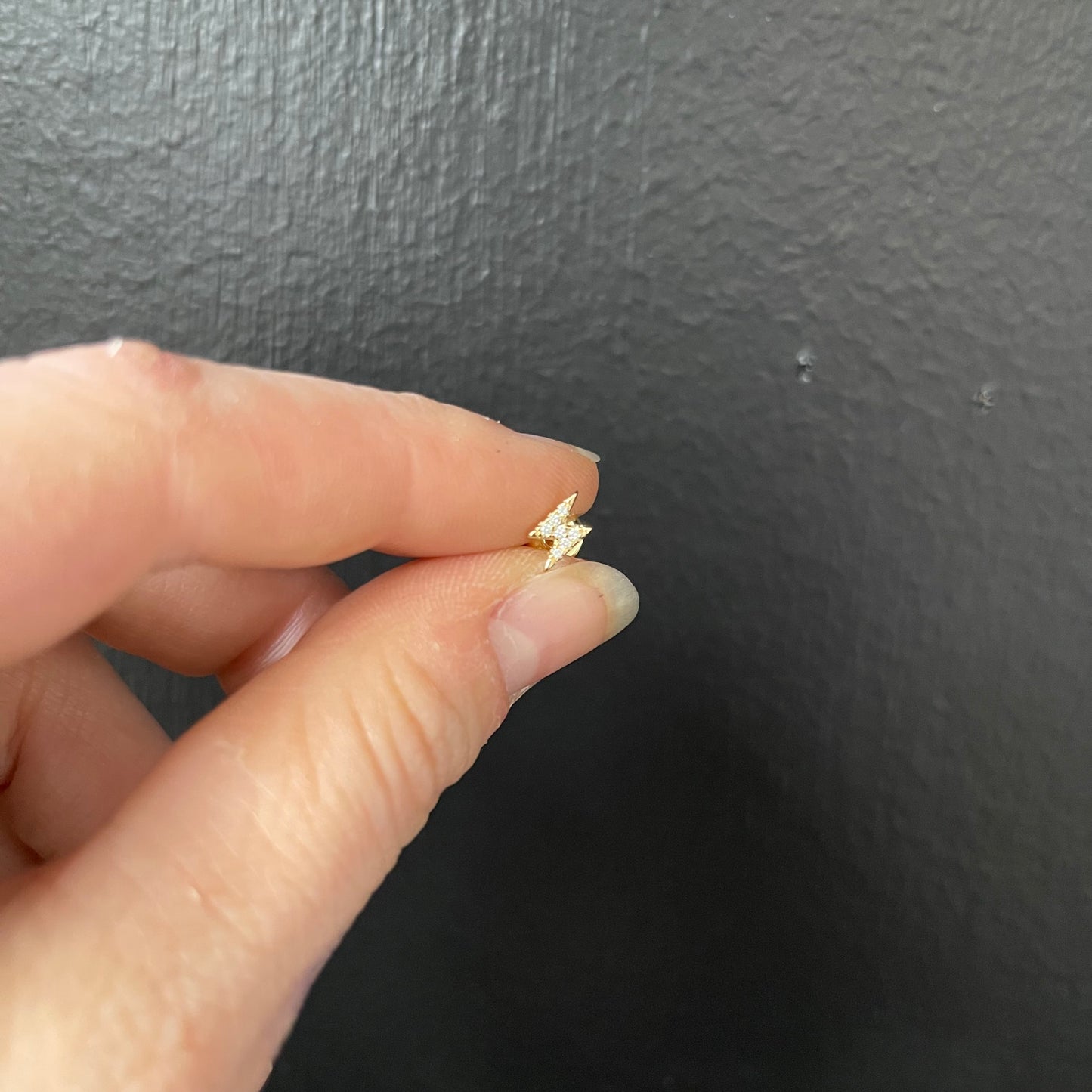 Gold lightening-shaped earring held between fingers against a dark background