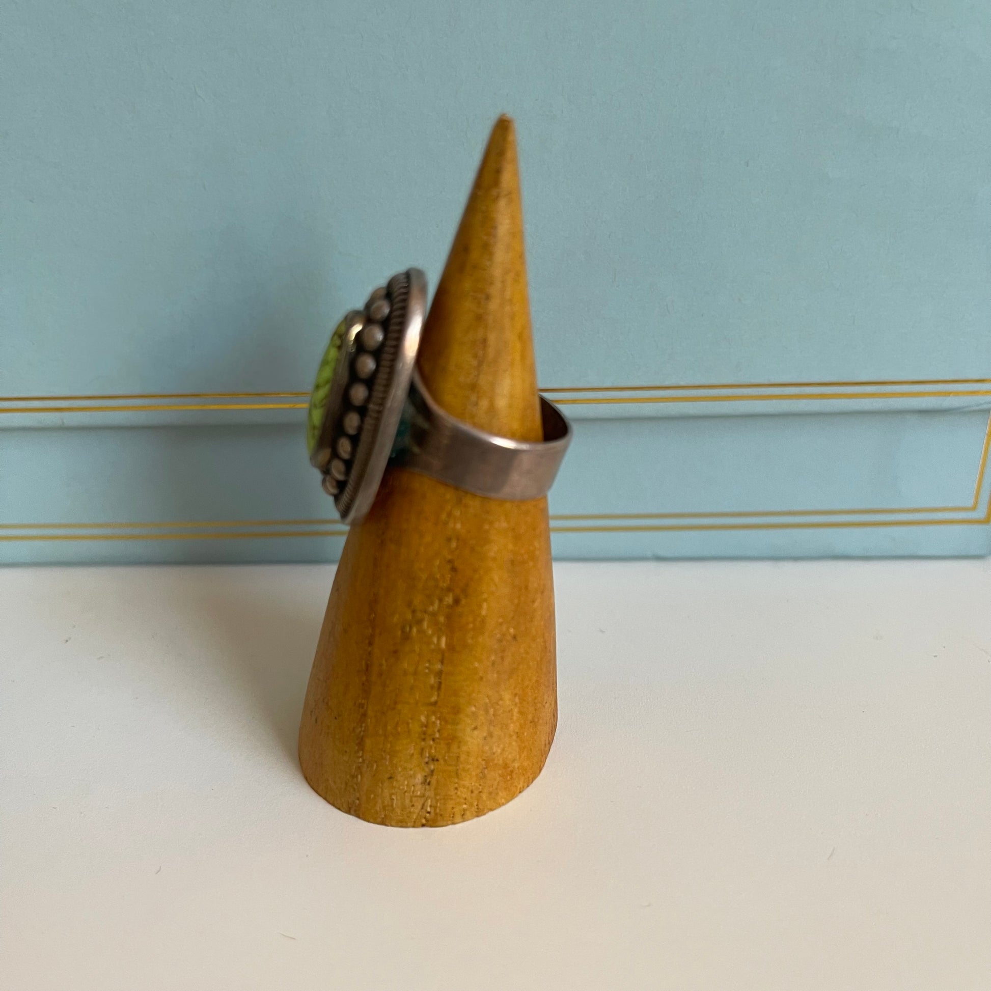Wooden cone-shaped ring holder with a silver ring on a light blue background