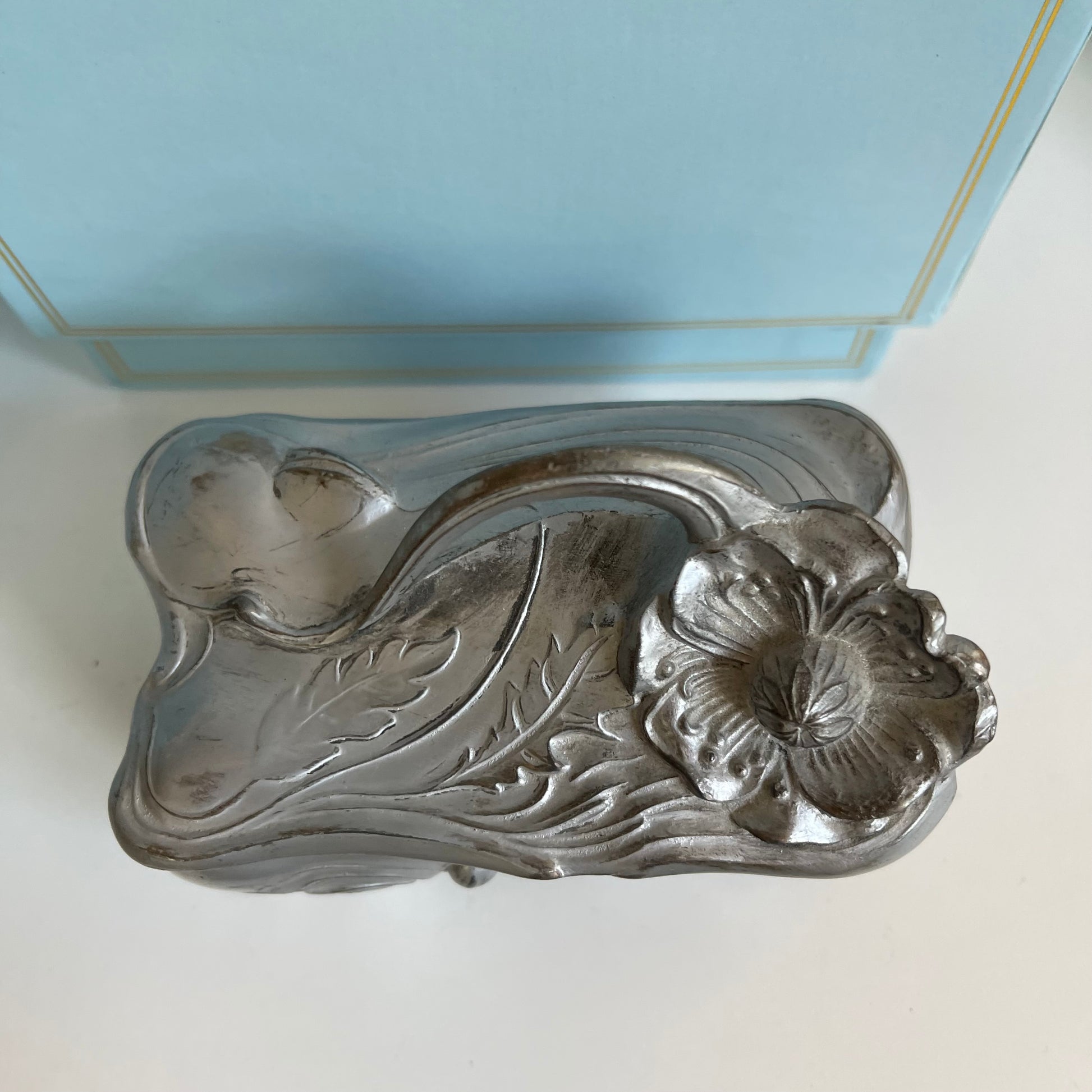 Decorative silver jewelry box lid with floral design on a white surface