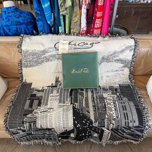 Decorative black and white Chicago skyline blanket with fringe and green Marshall Field’s box on a brown leather couch