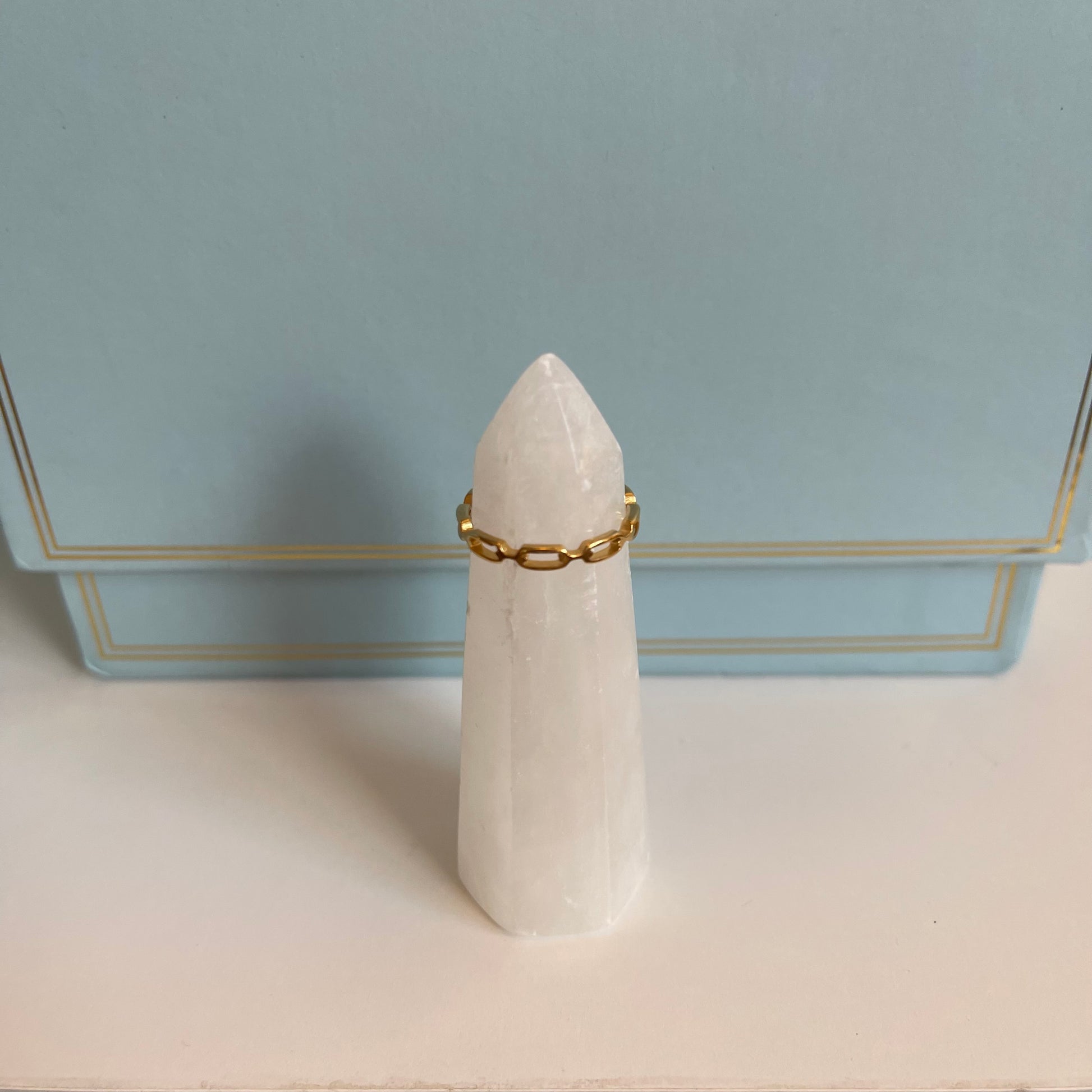 White stone with a delicate gold chain ring on a light blue background
