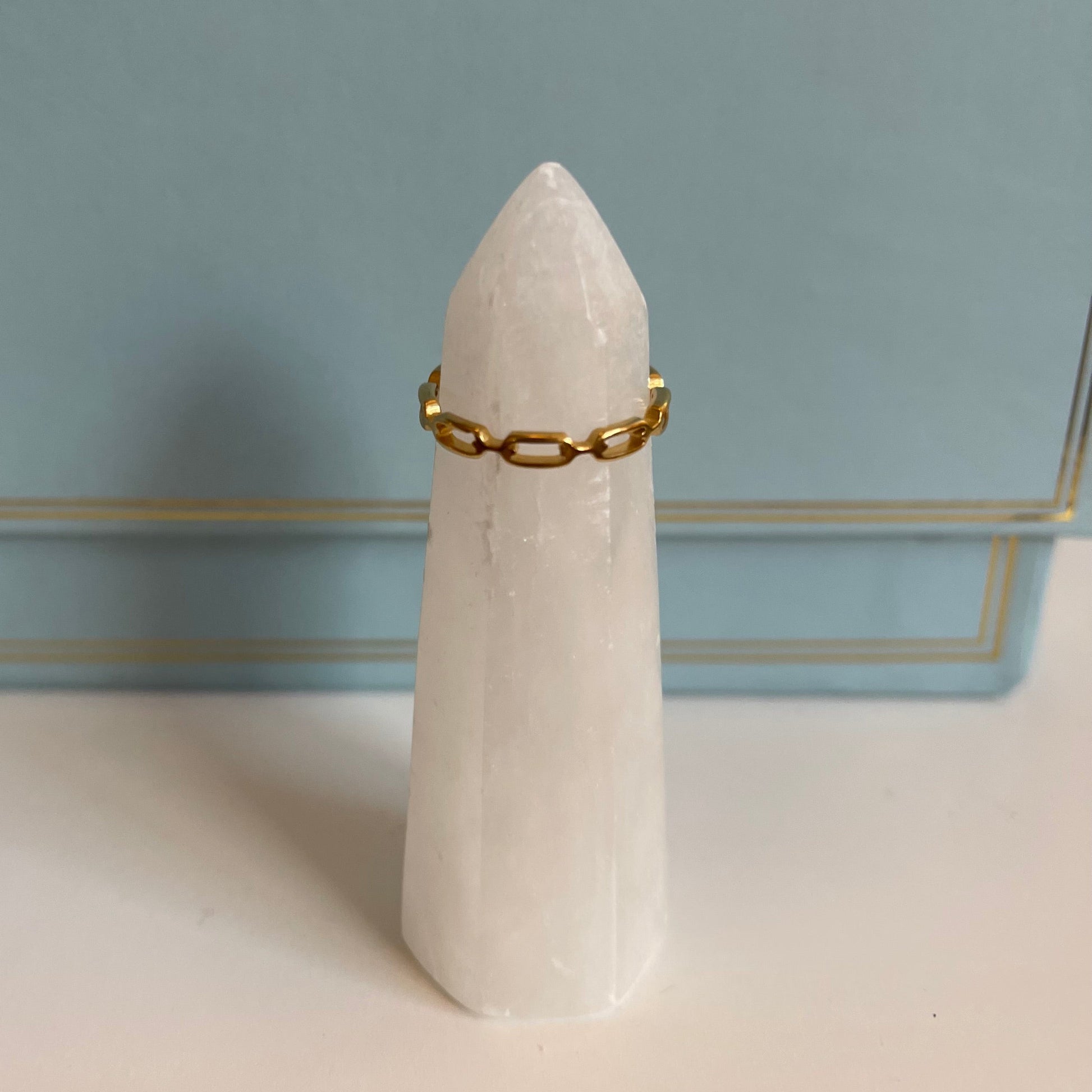 White stone with a delicate gold chain ring on a light blue background