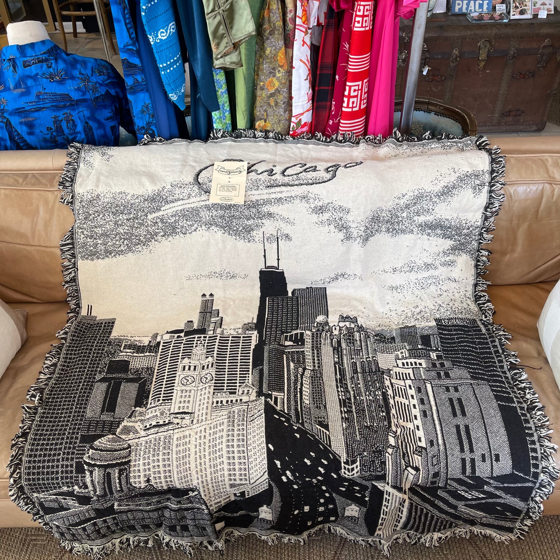 Decorative black and white blanket with Chicago skyline design and fringe on a brown leather couch