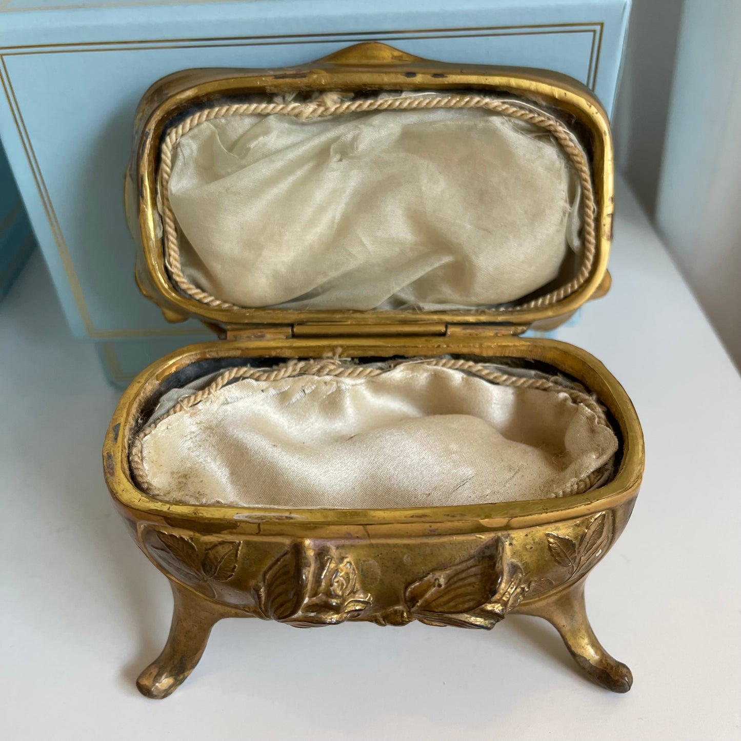 Gold jewelry box with white satin interior on a white surface
