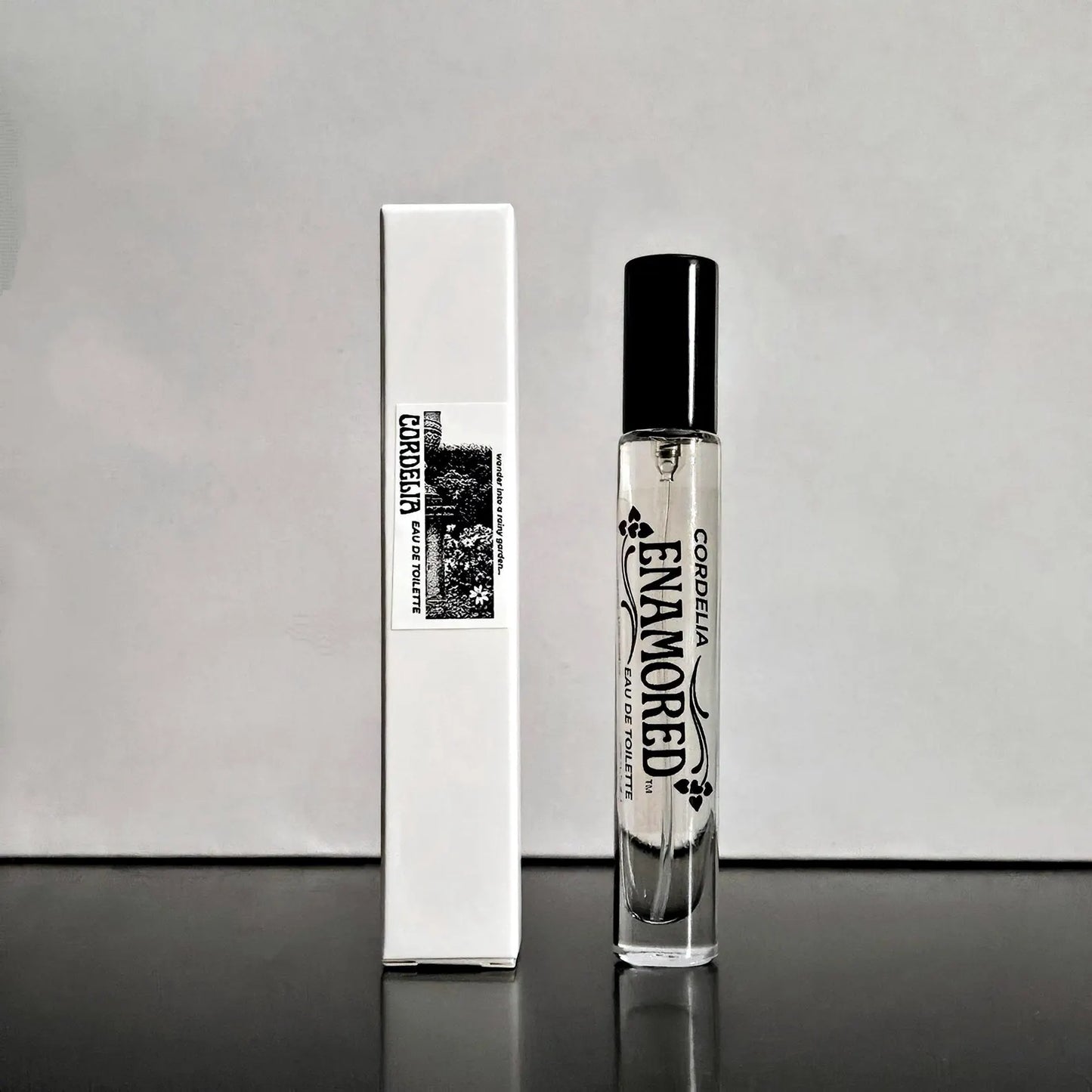 A clear glass perfume bottle with a black cap stands next to its white rectangular box. The bottle and box are printed with the brand name 'ENAMORED' and the scent name 'CORDELIA' in black text, with a small floral graphic.