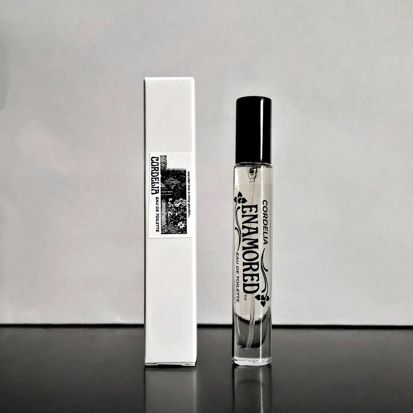 A clear glass perfume bottle with a black cap stands next to its white rectangular box. The bottle and box are printed with the brand name 'ENAMORED' and the scent name 'CORDELIA' in black text, with a small floral graphic.