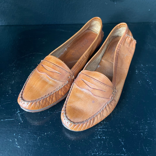Pair of worn-in chestnut brown leather penny loafers with white stitching by Cole Haan