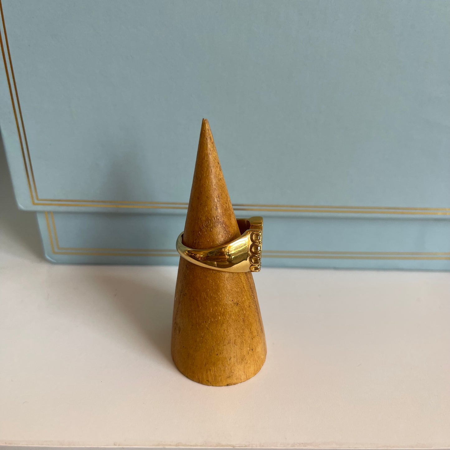 Side of thick gold ring on wooden cone-shaped ring display against light blue background